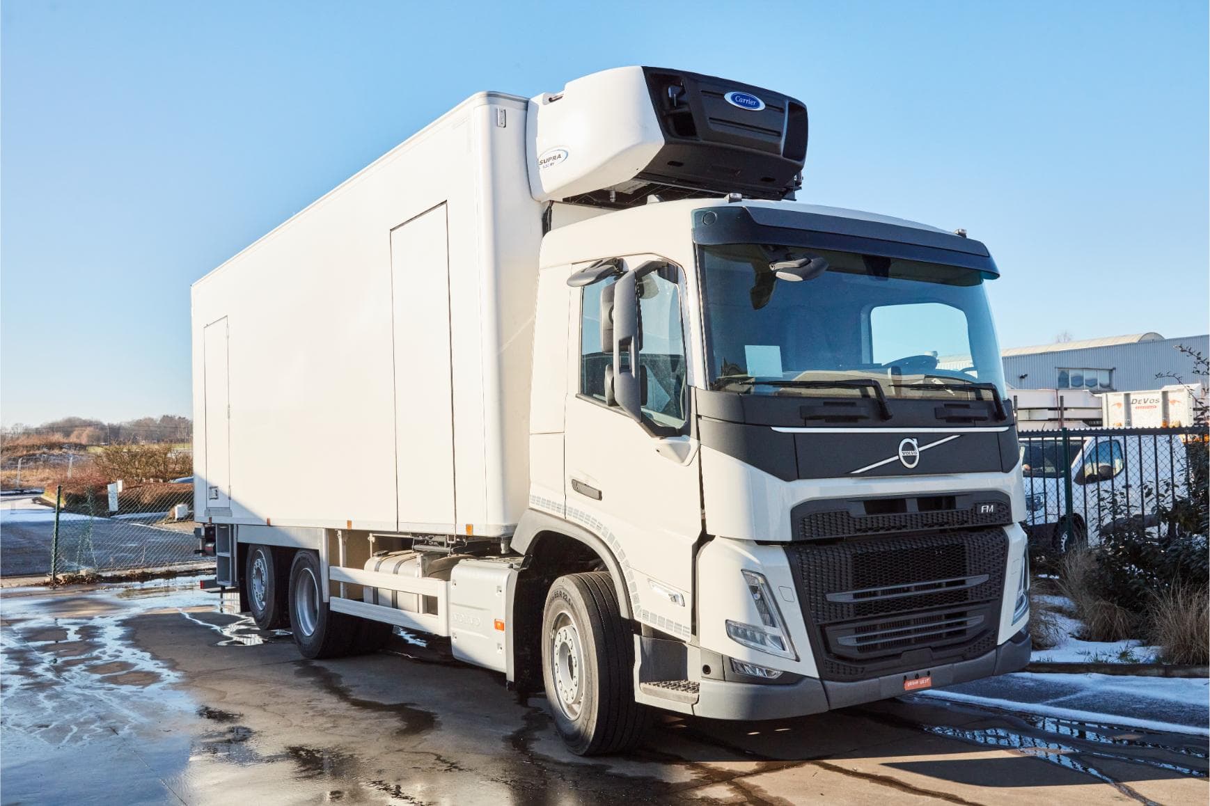 A white Volvo FM refrigerated truck with a Carrier Supra refrigeration unit on the roof, parked outside