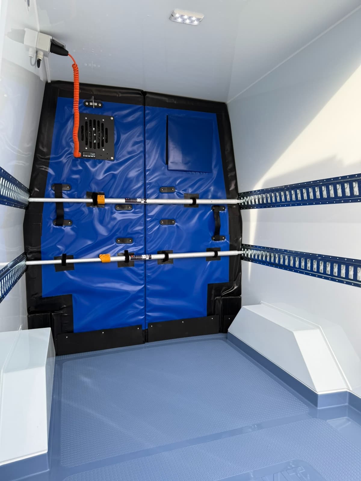 An extra freezer door in blue sheeting, with a fan, in a refrigerated van's load space