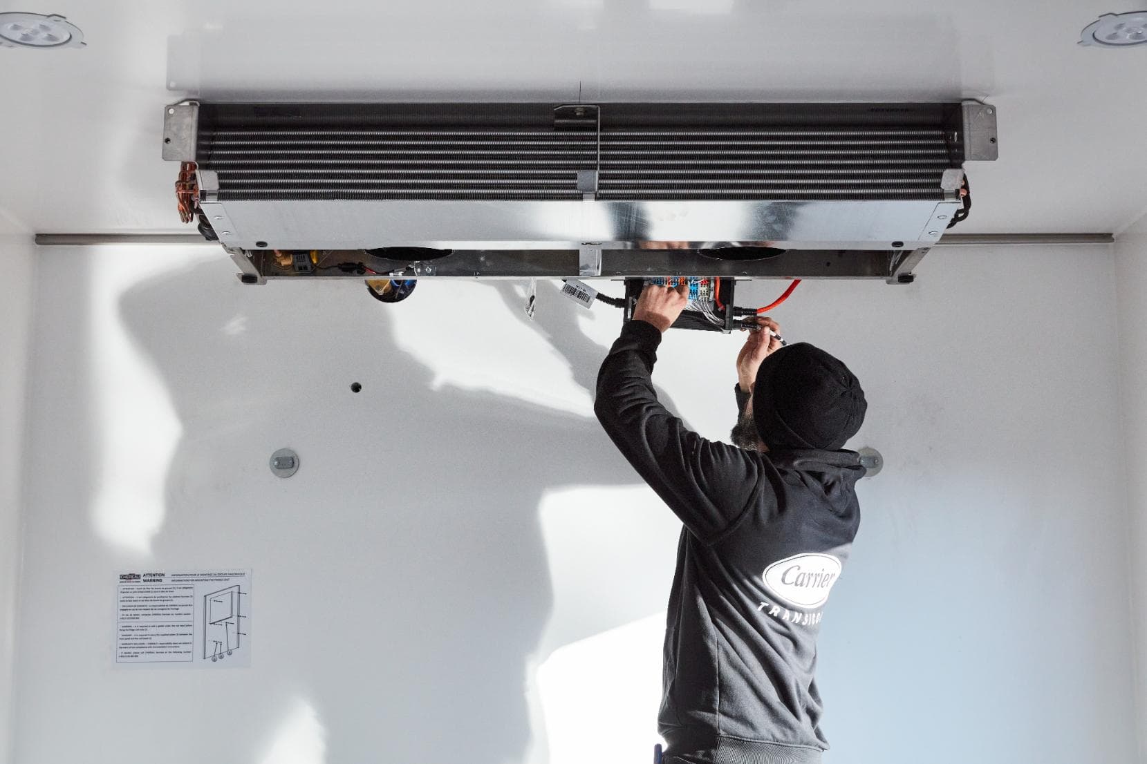 A technician wiring an evaporator to the ceiling of a white insulated load space