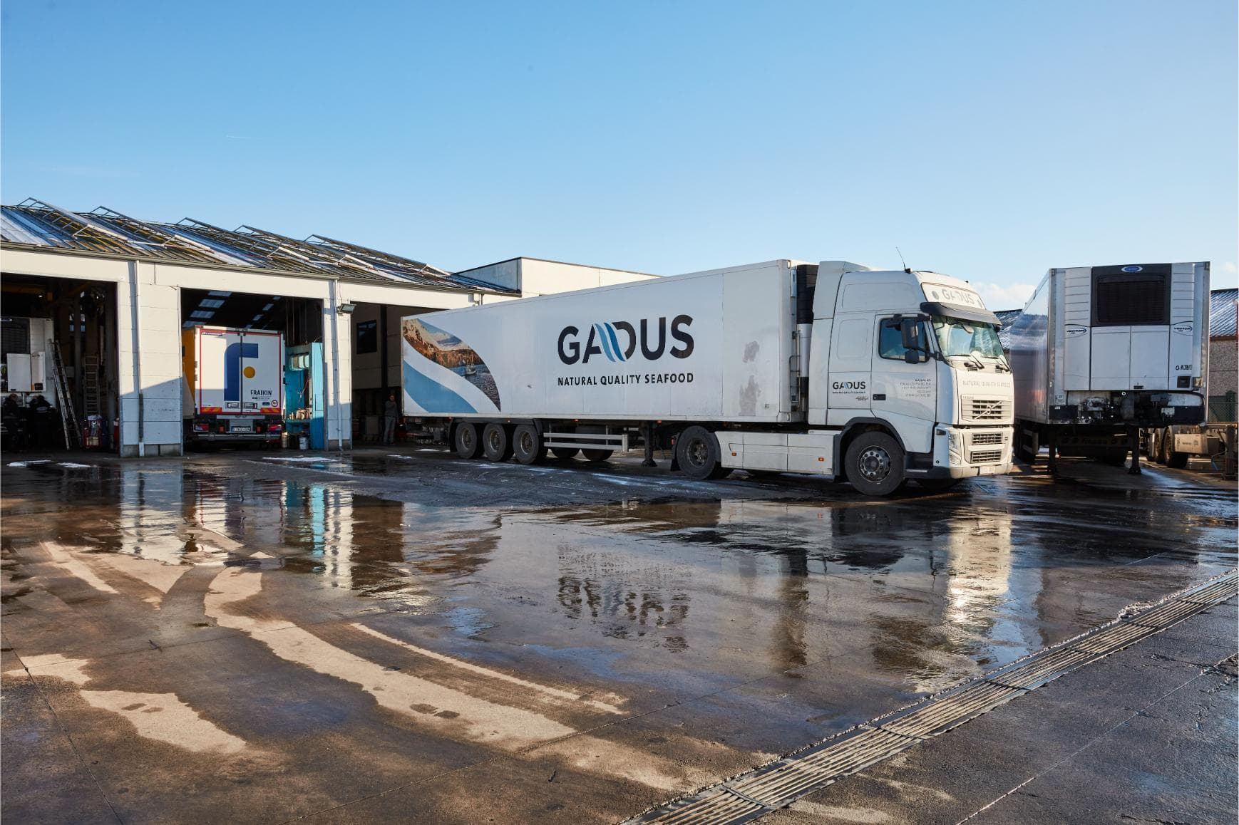 A white refrigerated trailer with a tractor unit in the Westcool yard, in front of the open workshop doors