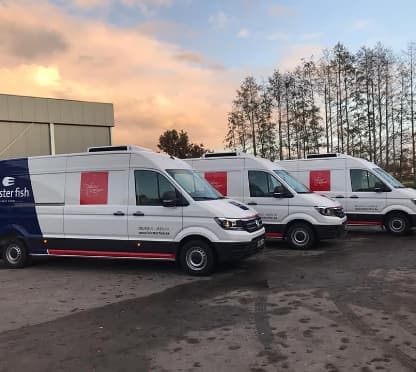 Three converted white panel vans with a refrigeration unit on the roof, parked in the yard